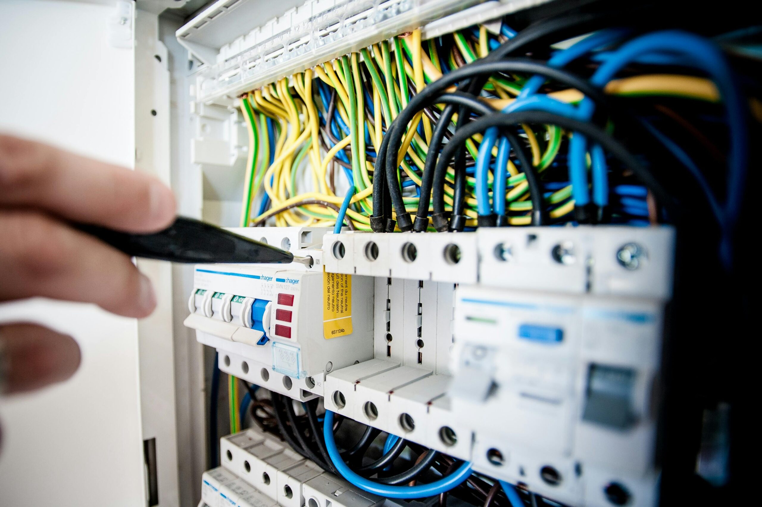 Services Hand of electrician working on a circuit breaker panel with colorful wires, ensuring safe electrical connections.
